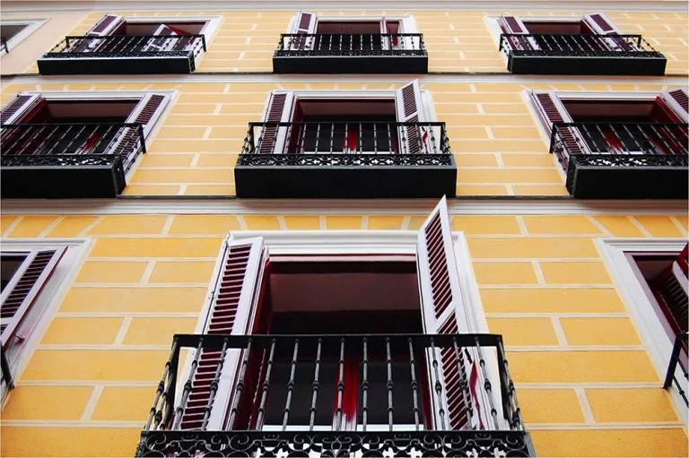 Representative hotel space: A low-angle view of a yellow building facade with windows and dark balconies.