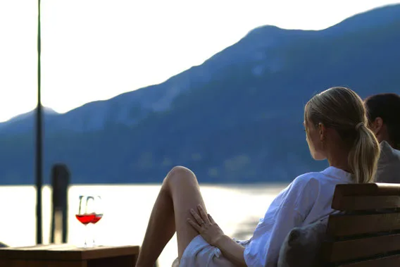 Representative hotel space: People sit at an outdoor table beside a lake with mountains in the background.