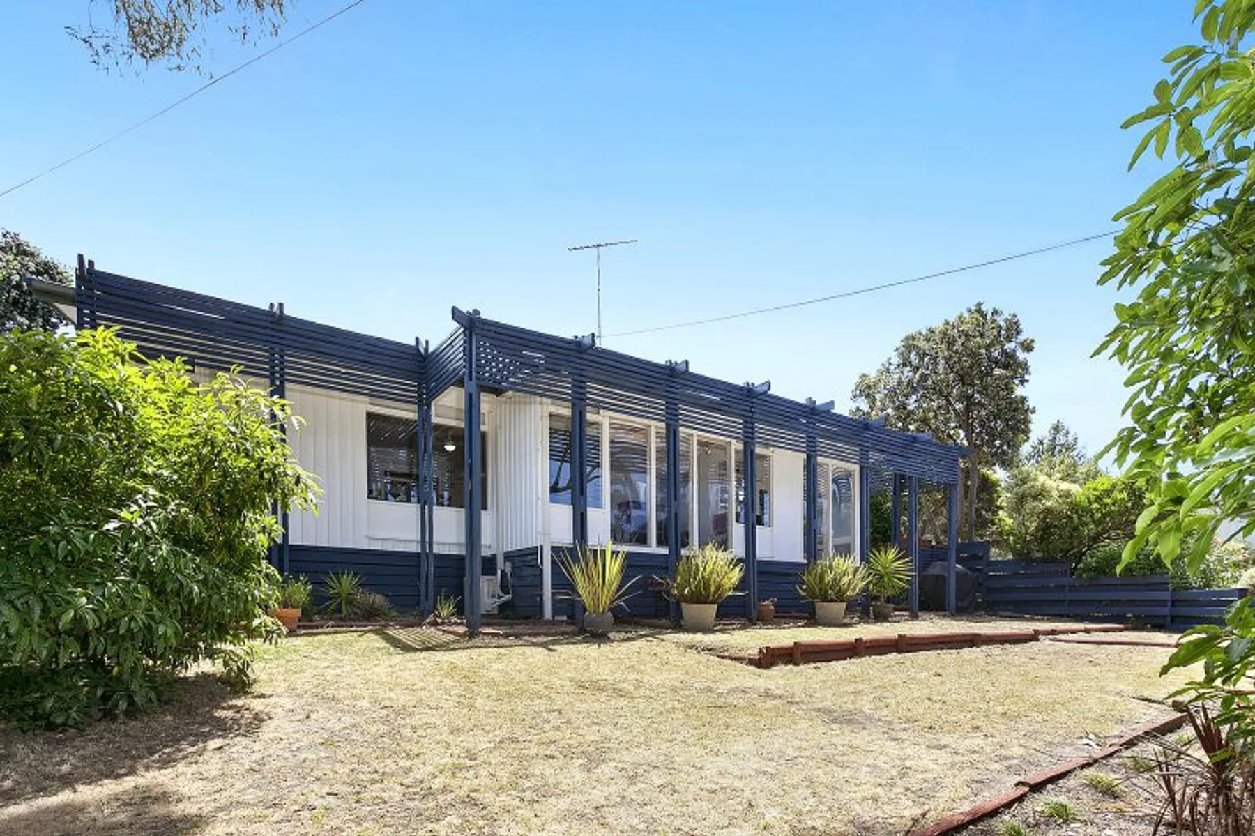 Una casa moderna baja con un patio largo sombreado y un jardín seco al frente.