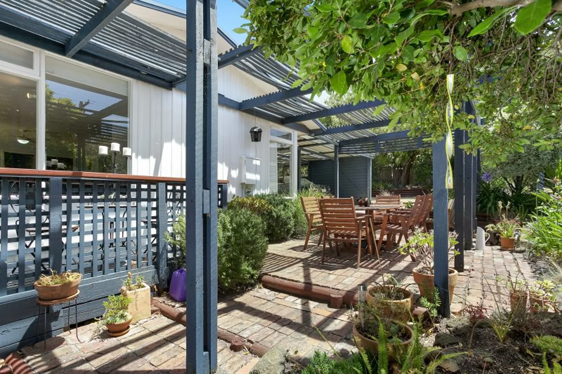 Un patio exterior sombreado con una mesa de comedor de madera y plantas frondosas.