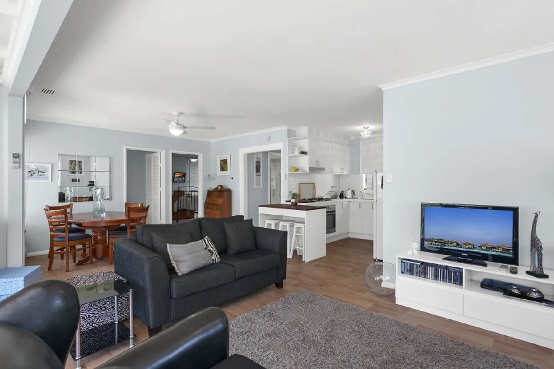 Una sala de estar de planta abierta con asientos oscuros, un televisor y una zona de cocina y comedor.