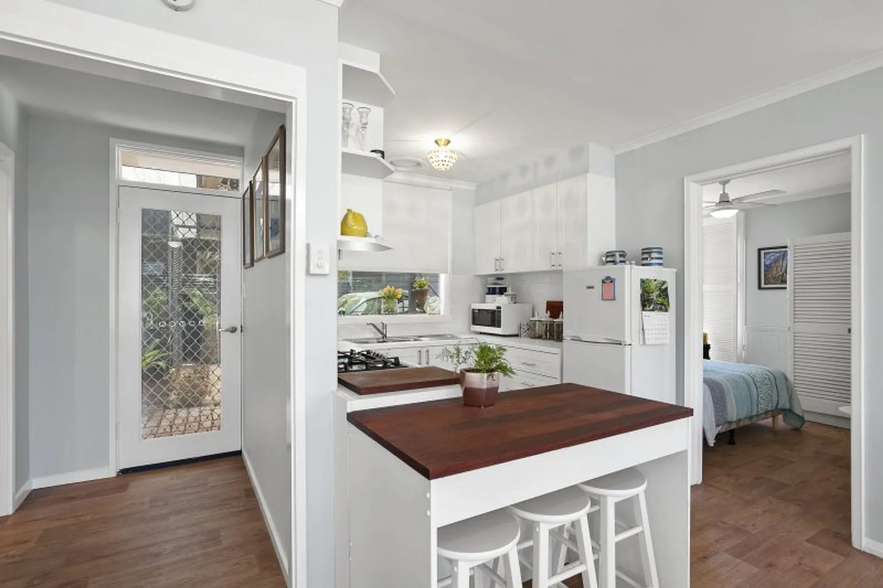 Una cocina abierta con una encimera oscura en la isla y un dormitorio visible por la puerta.