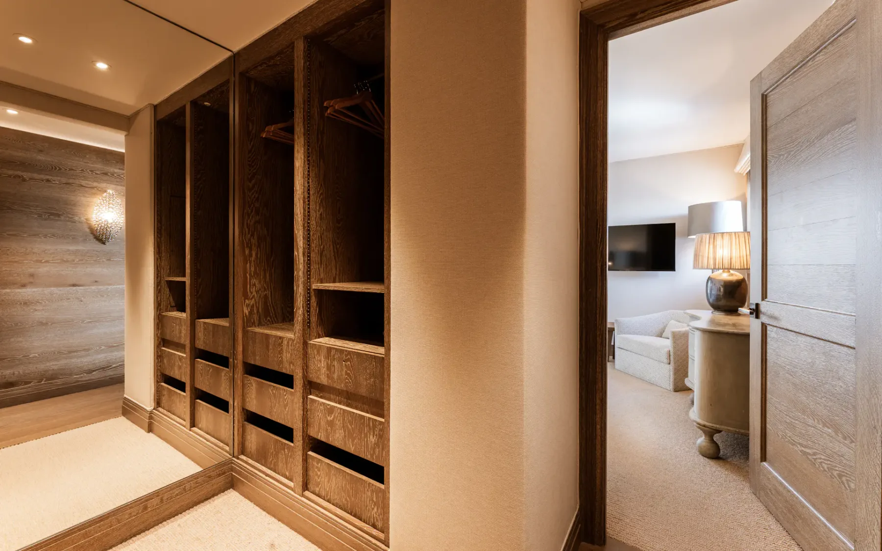 Zona de vestidor con armarios abiertos de madera y vista al área de descanso.