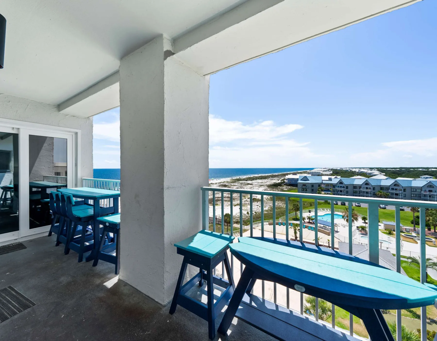 A covered balcony with blue seating overlooks the ocean and nearby buildings.