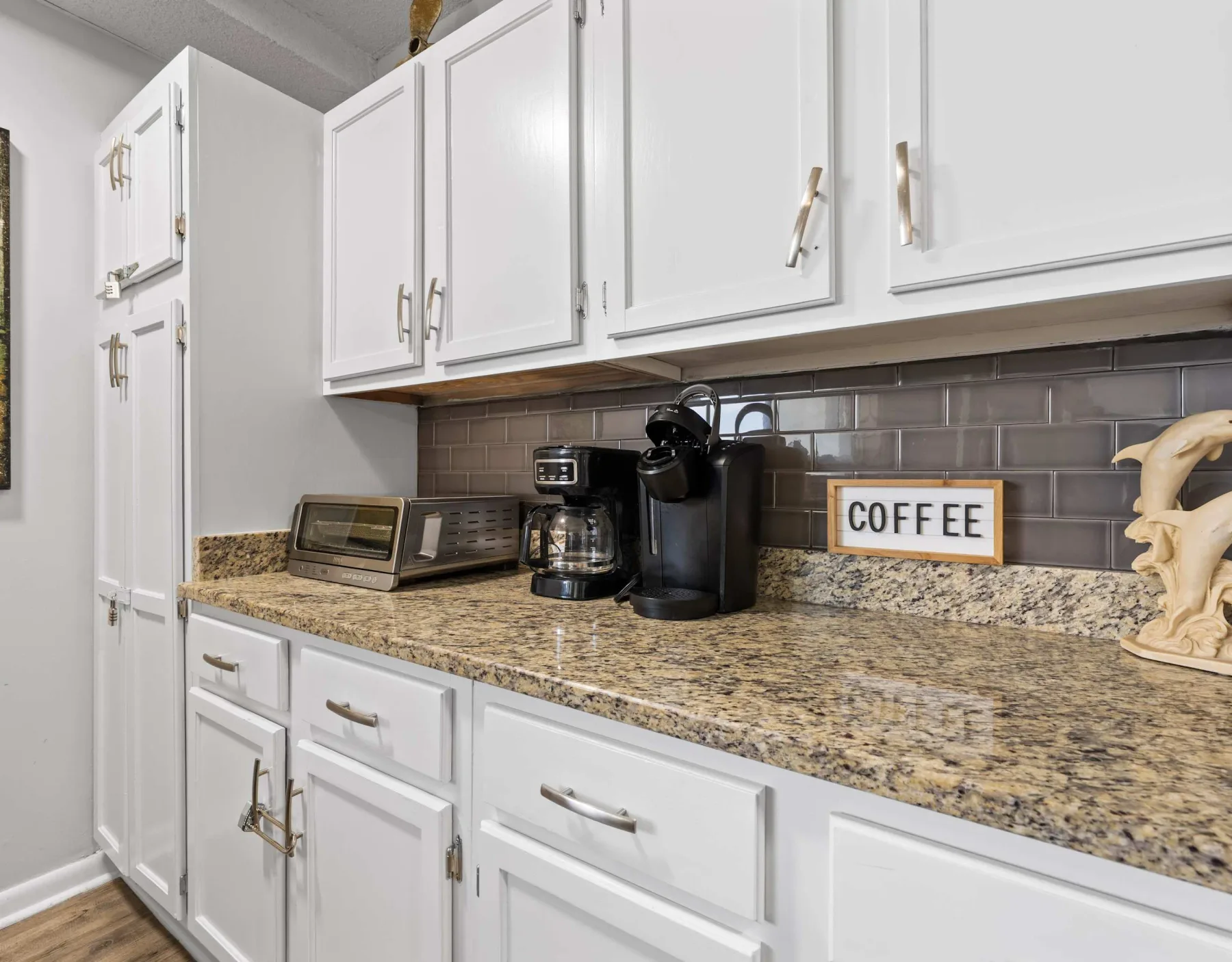 A kitchen counter with small appliances sits beneath white cabinets.