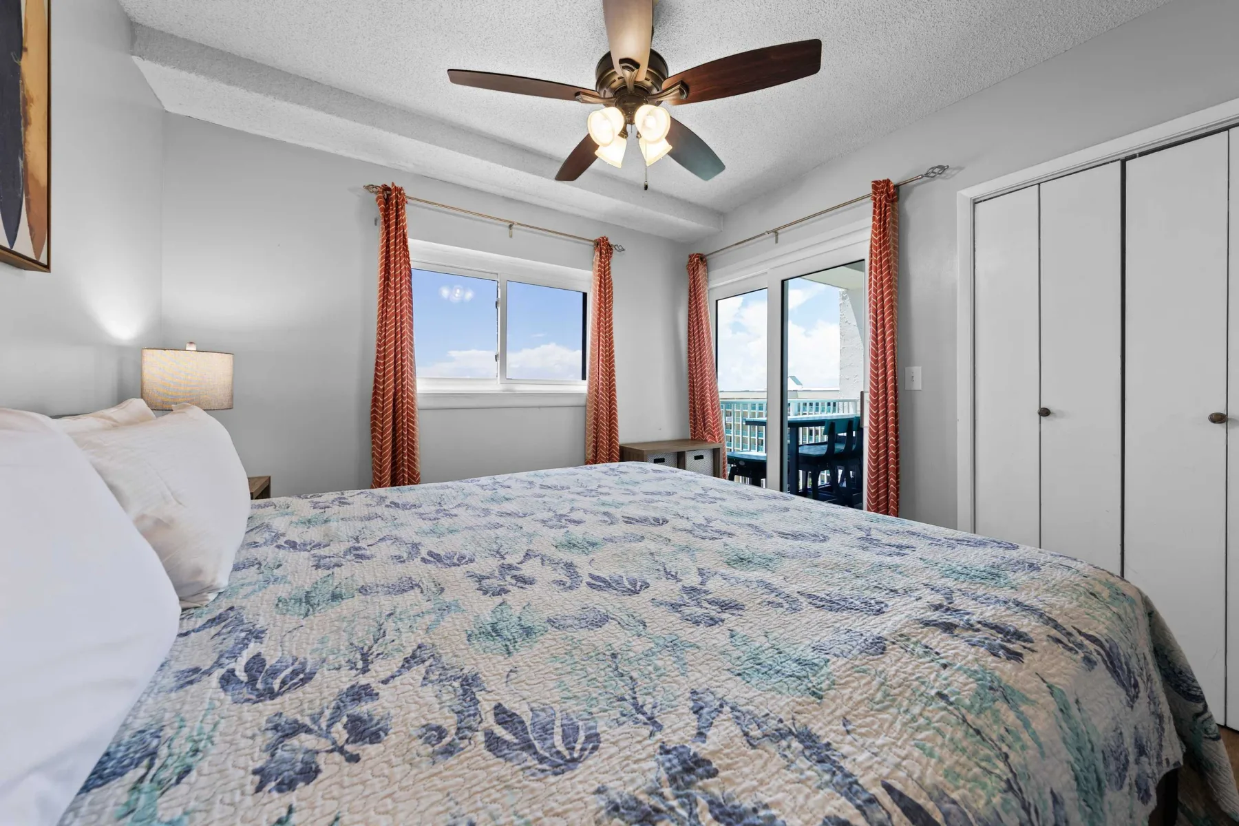 A bedroom with a floral bedspread, windows, and a sliding glass door.
