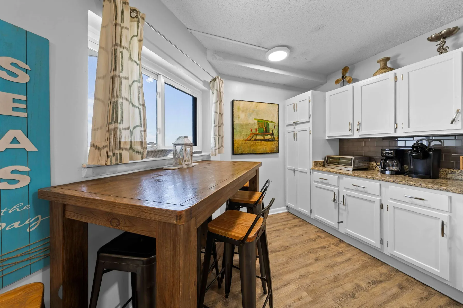 A kitchen with white cabinets, a wooden table, and large windows.