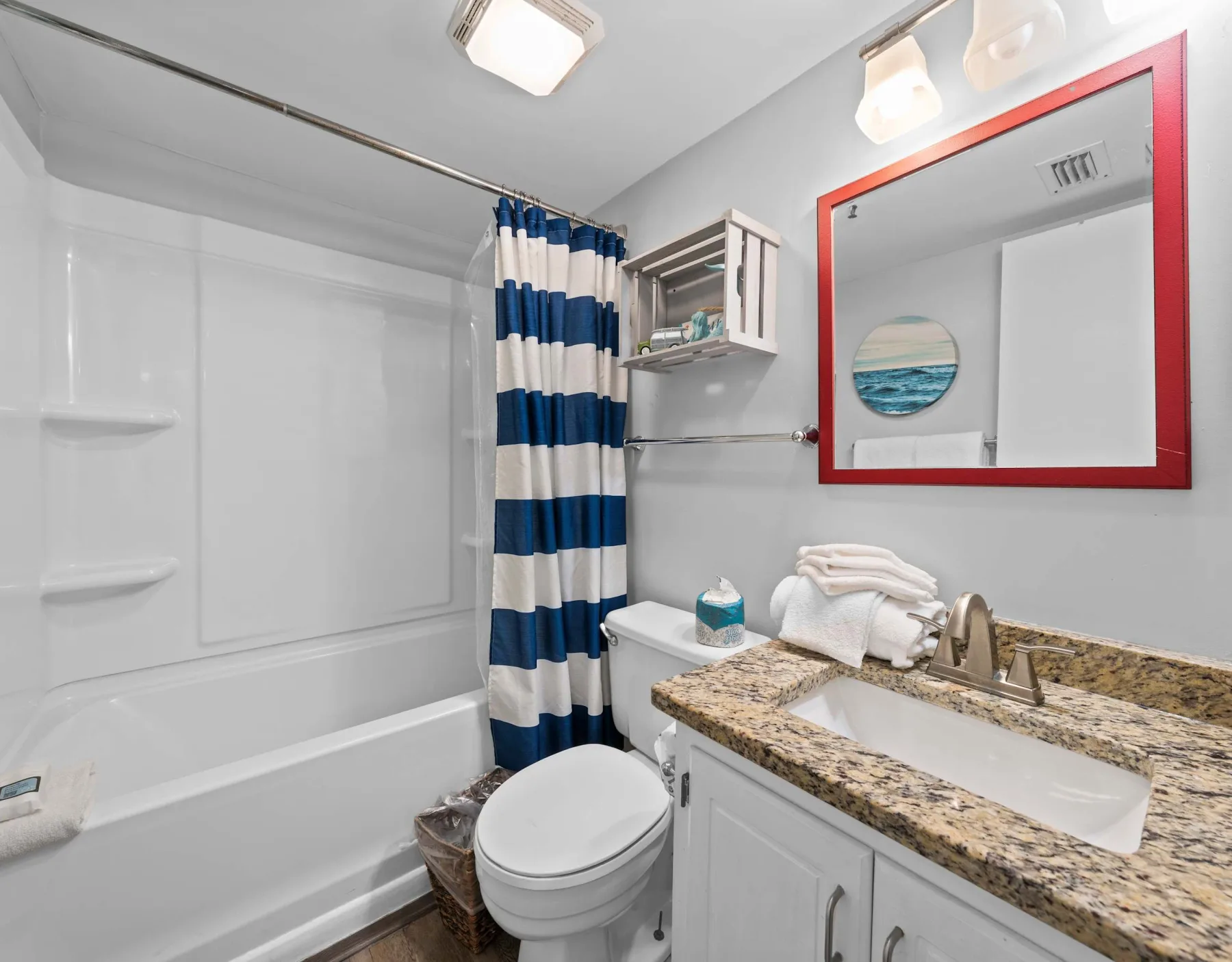 A bathroom with a bathtub, striped shower curtain, toilet, and sink vanity.