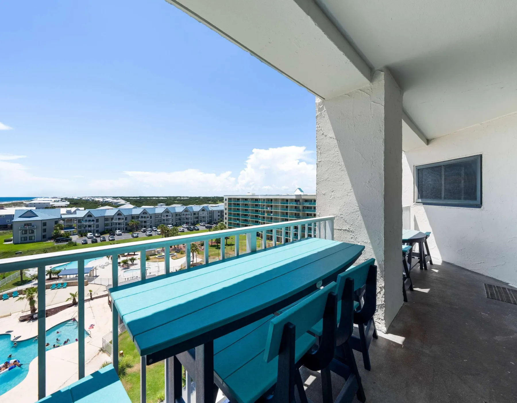 A balcony seating area overlooks a pool and nearby buildings.