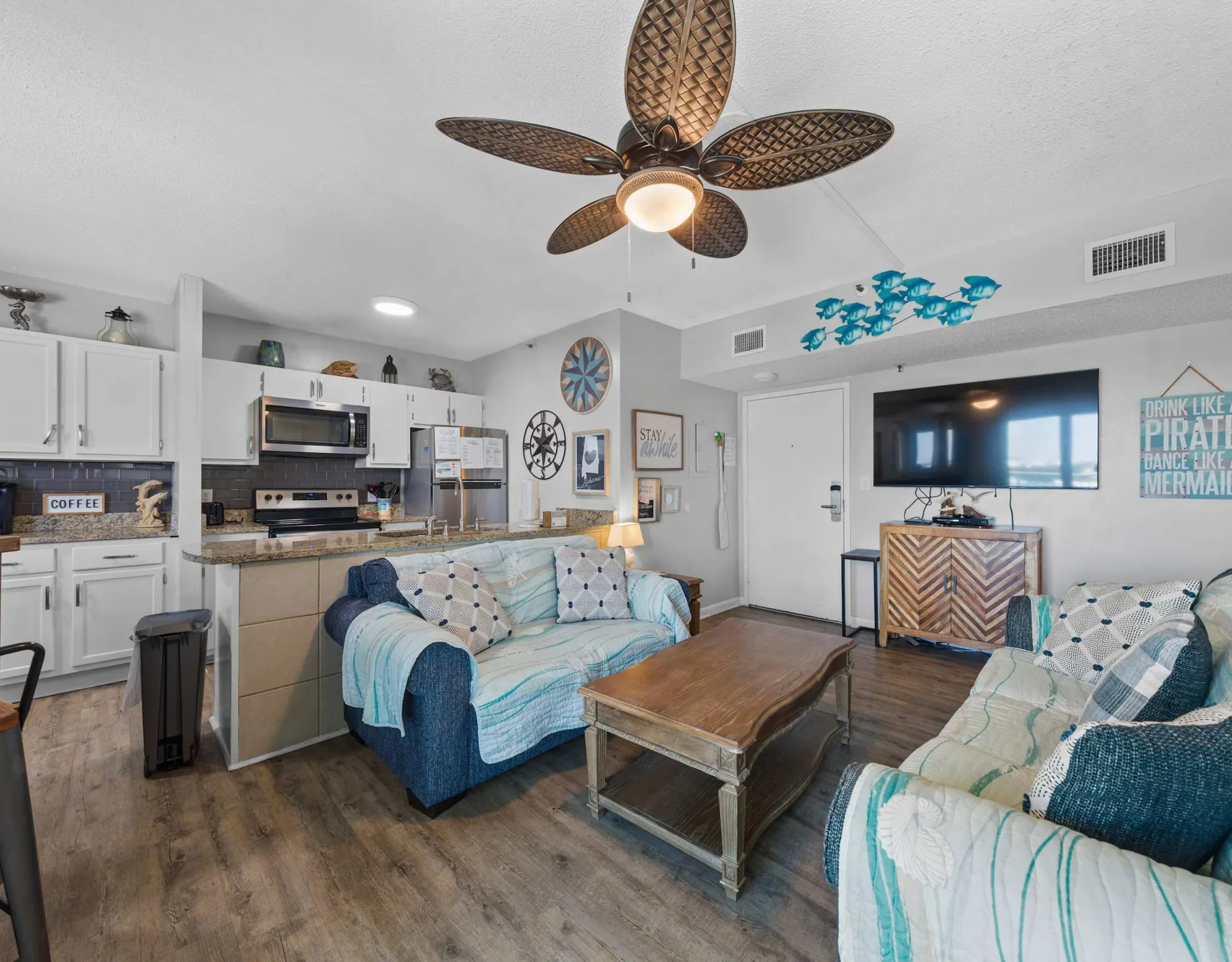 A living room with a kitchen area, blue seating, and a wooden coffee table.
