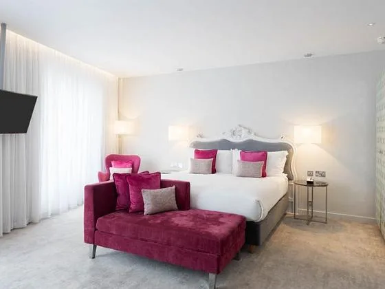 Espacio representativo del hotel: Un dormitorio luminoso con una cama blanca y asientos magenta.