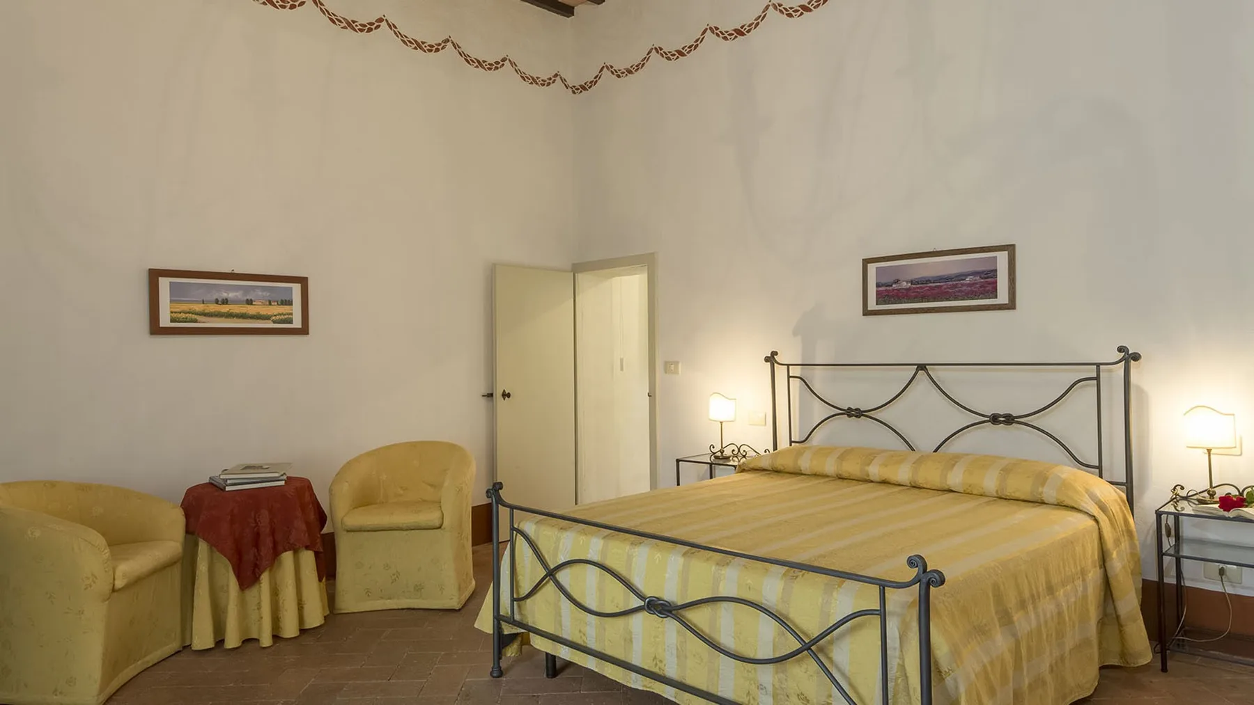 Un dormitorio con una cama de metal, ropa de cama amarilla y una pequeña zona de estar.