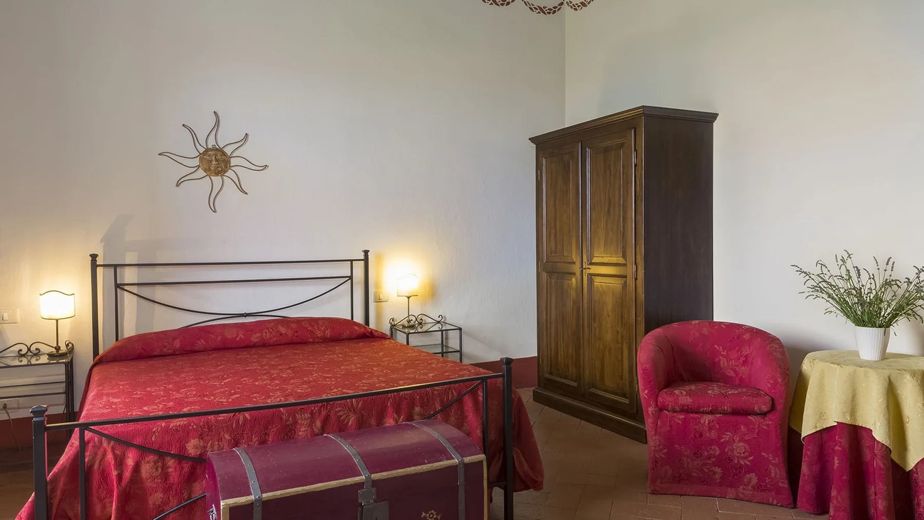 Dormitorio con una colcha roja, un armario oscuro y un sillón.