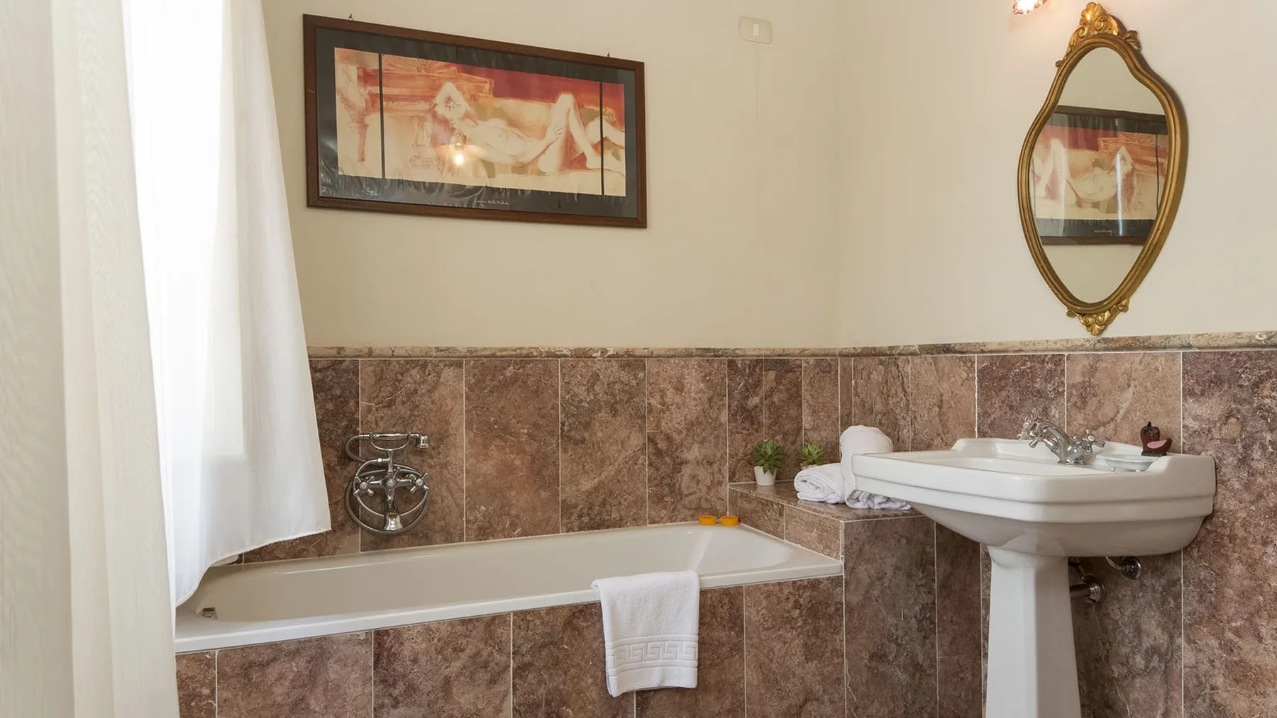 Un baño con bañera, lavabo con pedestal y cuadros enmarcados.