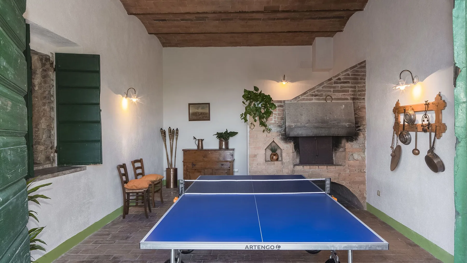 Una sala de recreación rústica con una mesa de ping-pong azul y vigas expuestas.