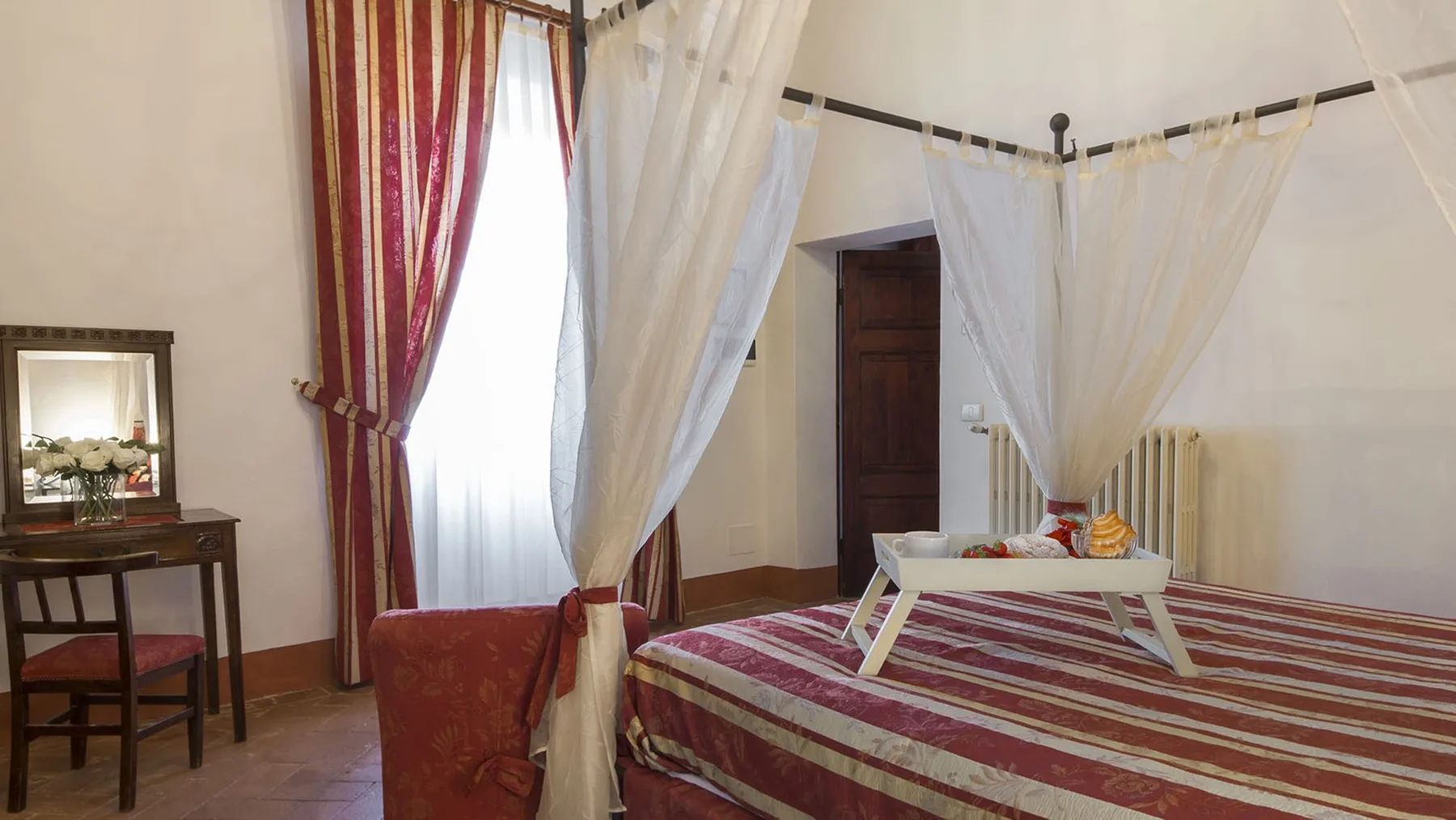 Un dormitorio con una cama a rayas y cortinas translúcidas alrededor de la zona de descanso.