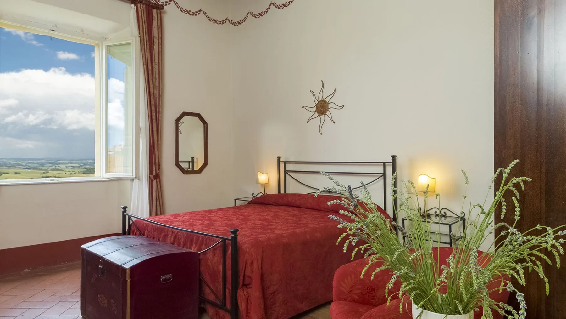 Un dormitorio con una cama cubierta de rojo, lámparas de noche y una ventana grande.
