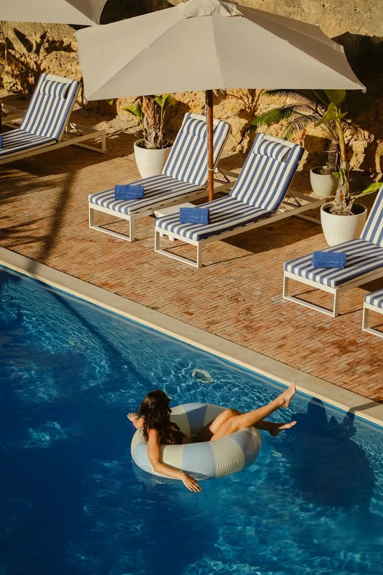 Espacio representativo del hotel: Una piscina junto a tumbonas a rayas y una sombrilla grande.