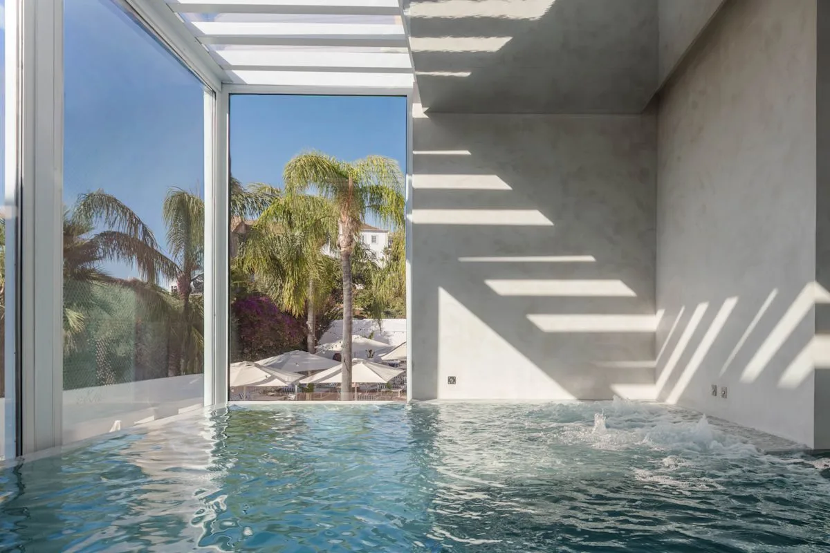 Espacio representativo del hotel: Una piscina cubierta está junto a grandes ventanas con vistas a palmeras.