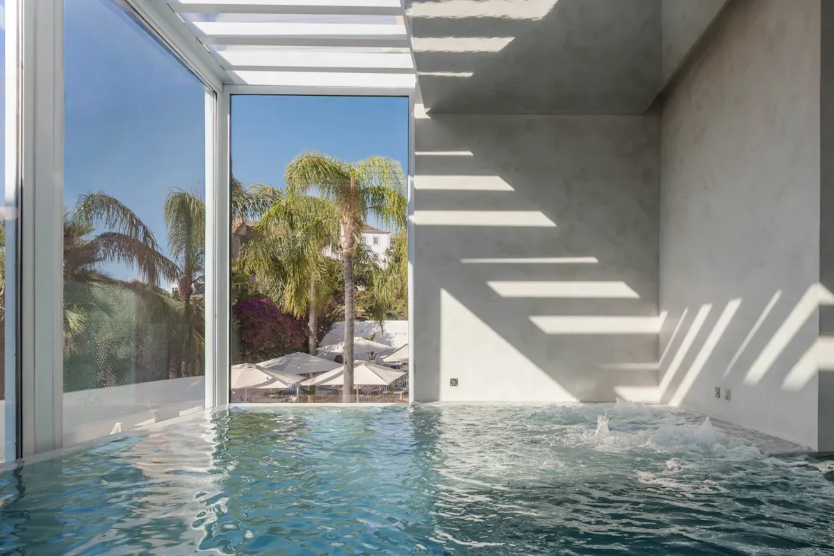 Espacio representativo del hotel: Una piscina interior está junto a grandes ventanales con vistas a palmeras.