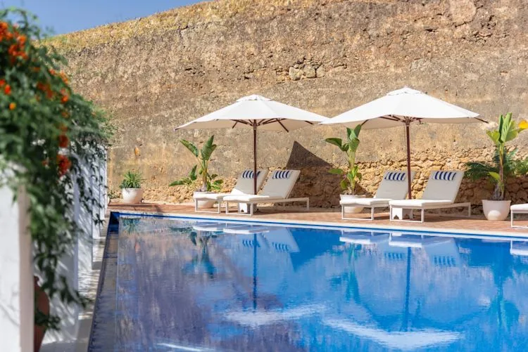 Espacio representativo del hotel: Una piscina al aire libre está junto a asientos reclinables y sombrillas blancas.