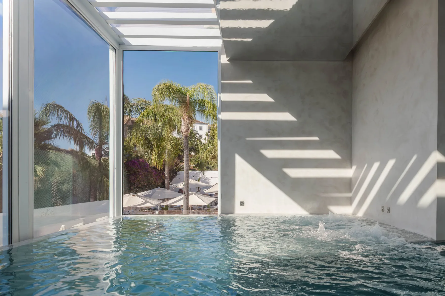Espacio representativo del hotel: Una piscina cubierta está junto a ventanales con vistas a palmeras.