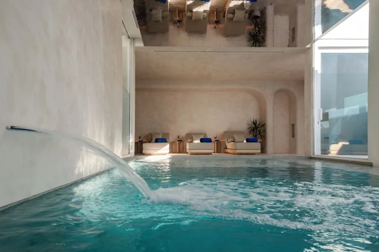 Espacio representativo del hotel: Una piscina cubierta con un elemento curvo de agua y asientos junto a la pared del fondo.