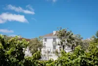 Espacio representativo del hotel: Un edificio blanco de varias plantas se alza entre árboles frondosos bajo un cielo azul despejado.