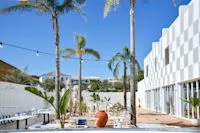 Espacio representativo del hotel: Un edificio moderno se encuentra junto a un patio ajardinado con palmeras y asientos.