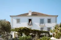 Espacio representativo del hotel: Una casa blanca con ventanas con contraventanas se alza tras arbustos del jardín.