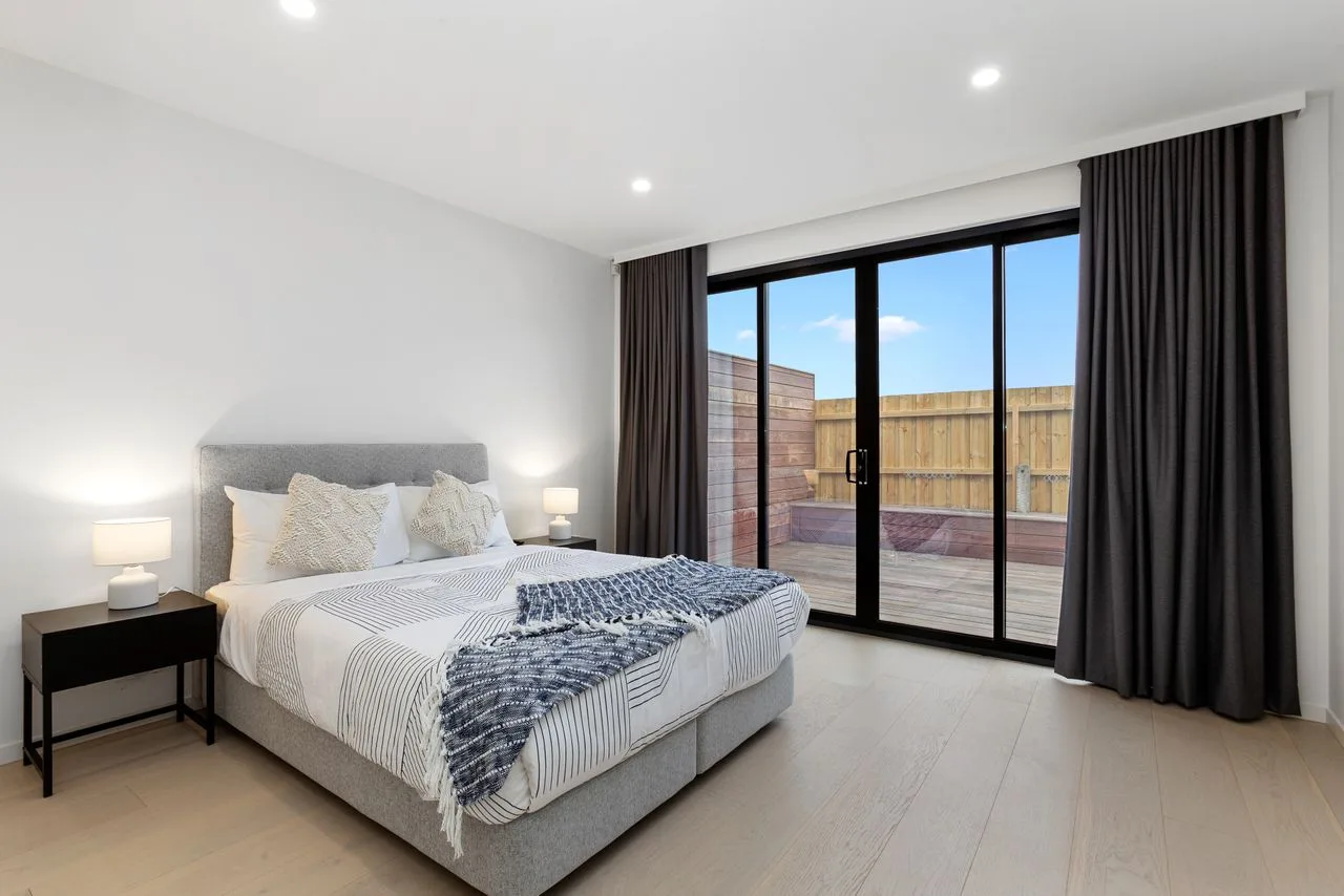 Un dormitorio luminoso con una cama junto a grandes puertas de vidrio que dan a un patio.
