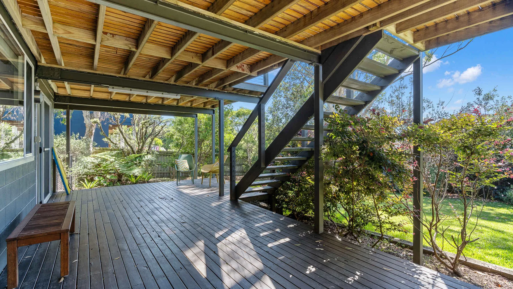 Una terraza exterior cubierta con una escalera de madera y vistas al jardín.