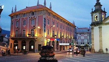 Espacio representativo del hotel: Un edificio iluminado de aspecto histórico da a una plaza pavimentada al anochecer.