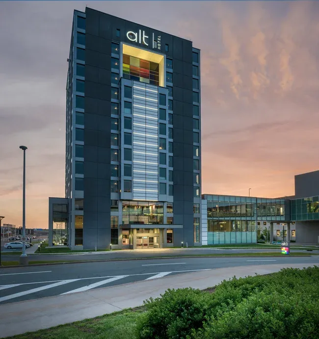 Representative hotel space: A modern hotel building with a glass-fronted entrance stands beside a road at dusk.