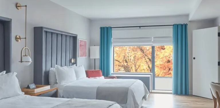 Representative hotel space: A bright bedroom with beds and a large window framed by blue curtains.