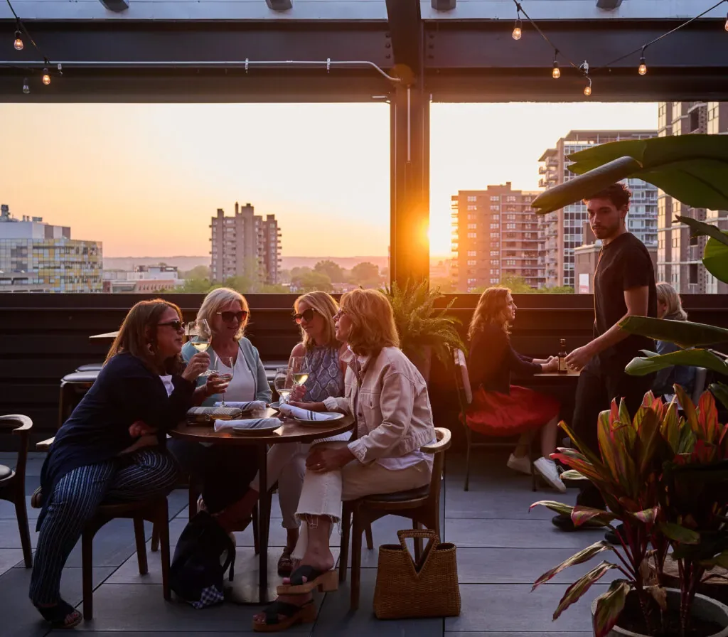 Representative hotel space: People gather around tables on a rooftop terrace at sunset.