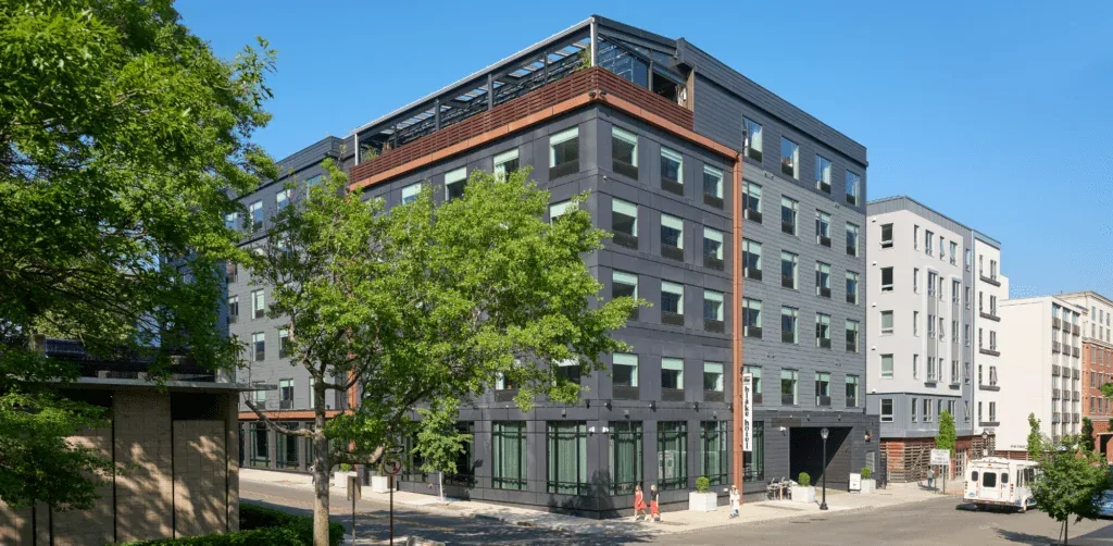 Representative hotel space: A modern multi-story building stands along a sunny street with trees nearby.
