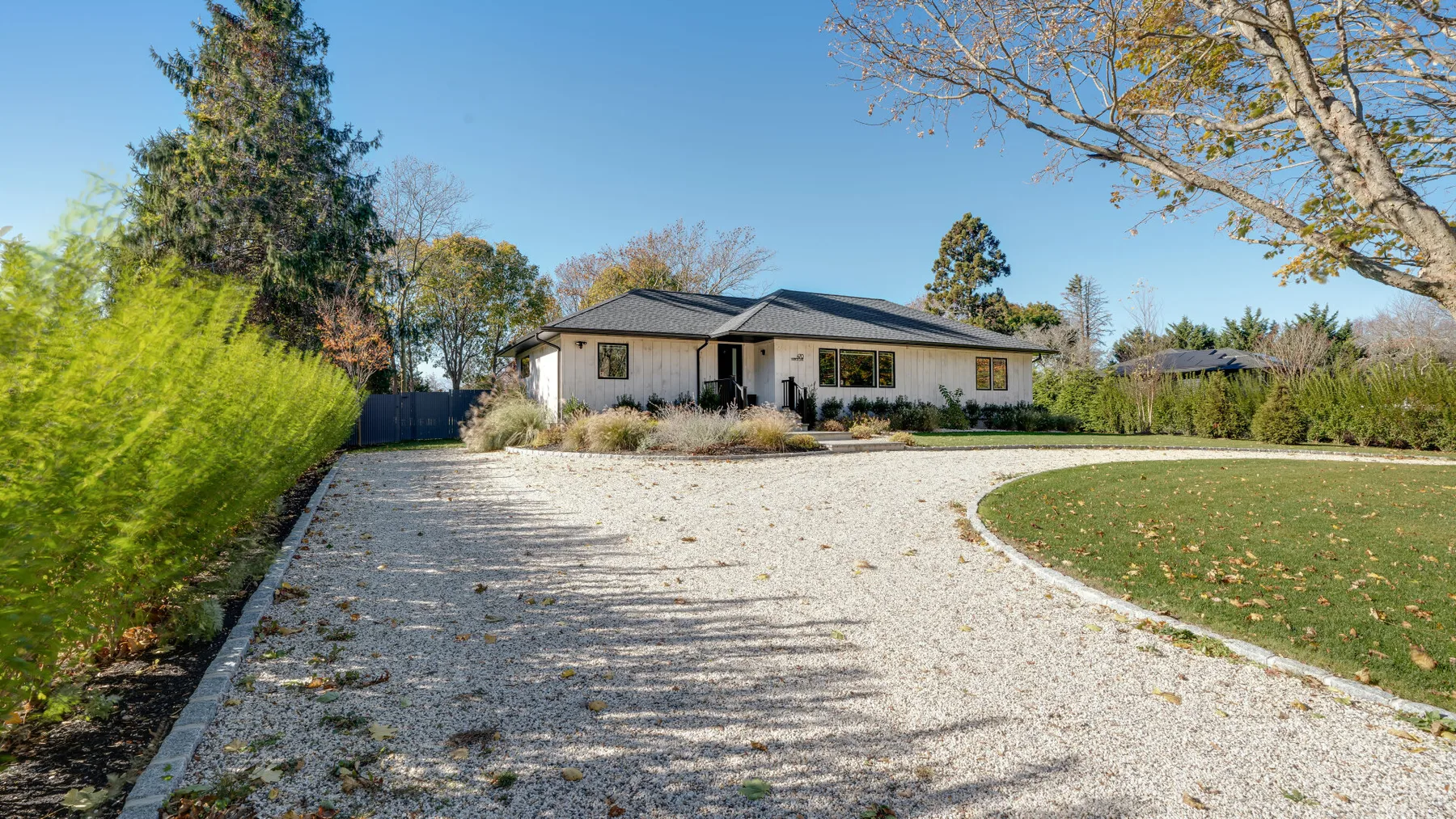 A single-story house stands beyond a broad gravel driveway and lawn.