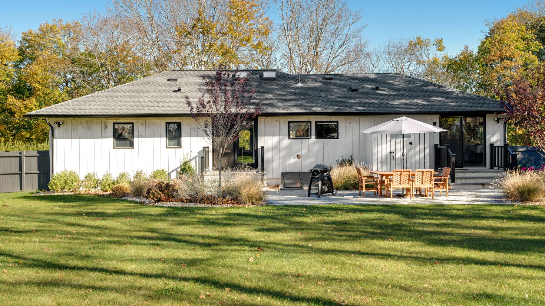 A single-story house with a lawn and outdoor seating beneath a patio umbrella.