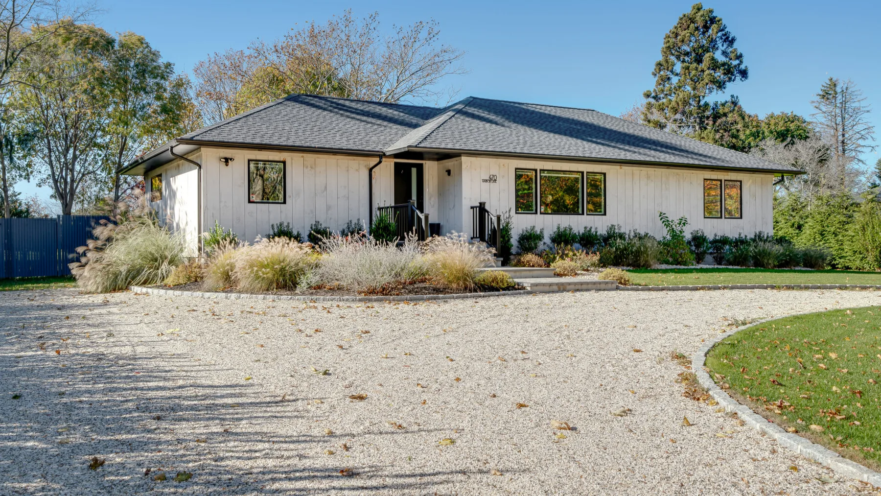 A single-story house with a dark roof stands behind a broad gravel driveway.