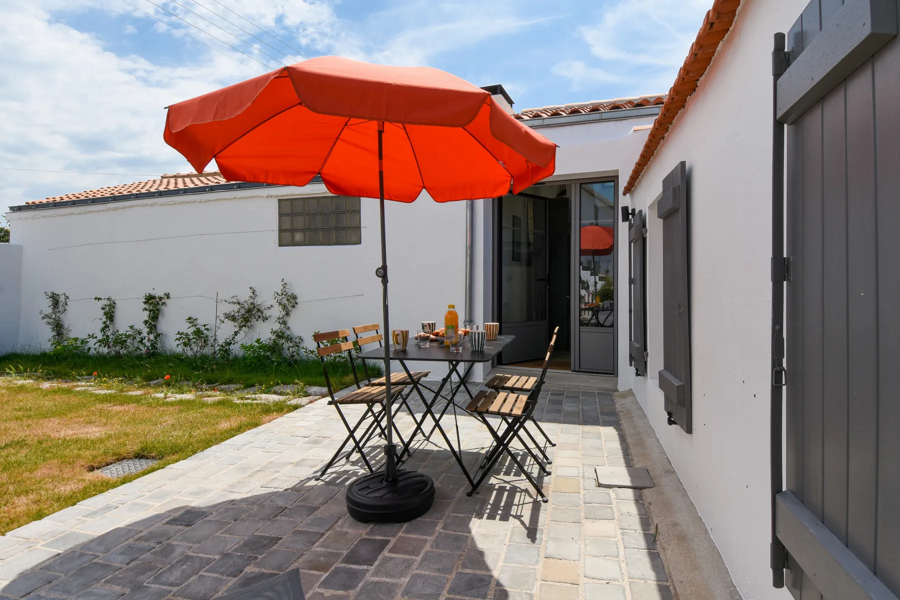 A paved outdoor patio has a table and seating beneath a red umbrella.