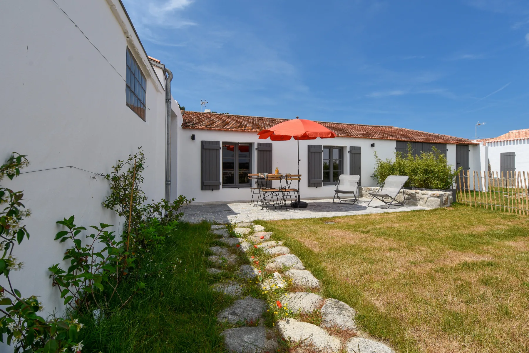 A sunny courtyard with patio seating, an umbrella, and a stone path.