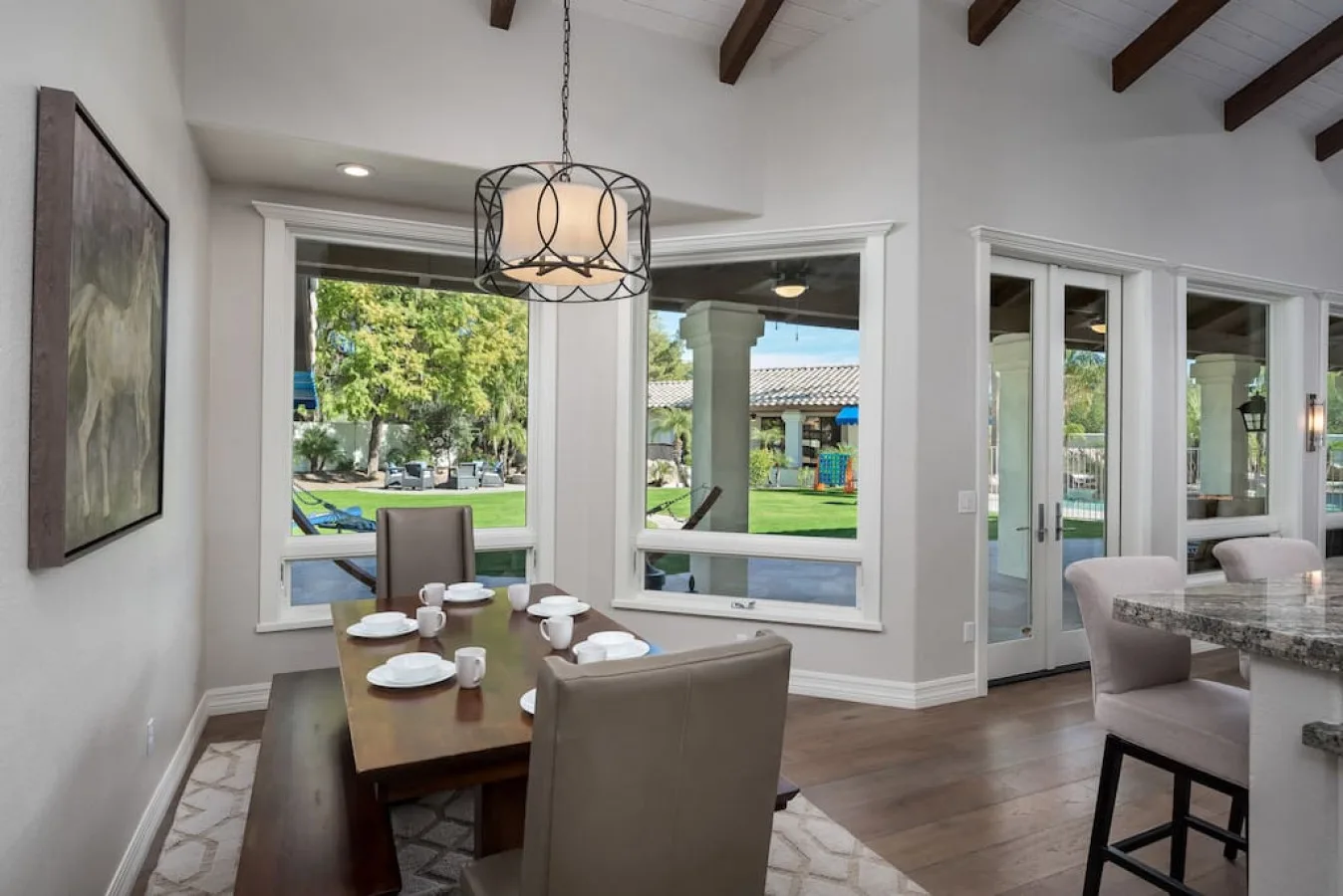 Un comedor con mesa y sillas junto a grandes ventanas con vistas a un jardín.