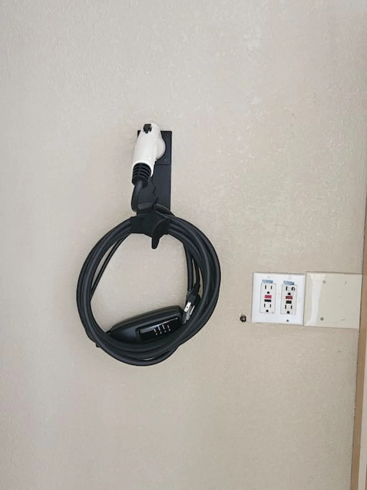 Un cable de carga enrollado está junto a una toma de corriente en la pared.