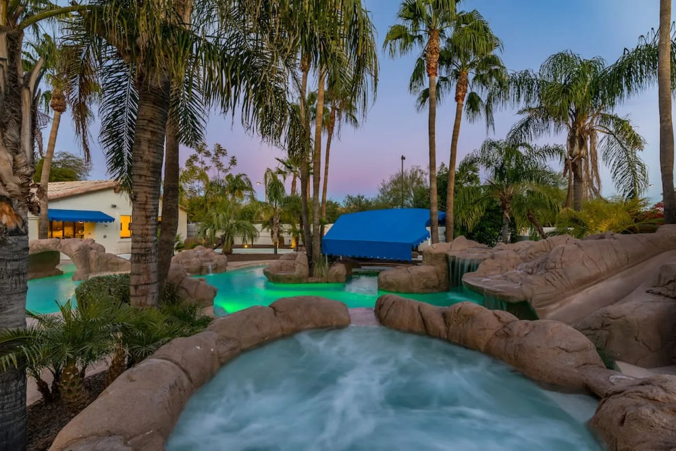 Una piscina y un spa burbujeante están rodeados de palmeras y rocas.