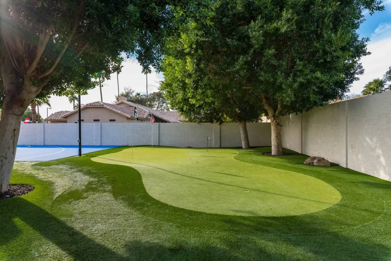 Una cancha exterior cercada con césped verde y grandes árboles de sombra.