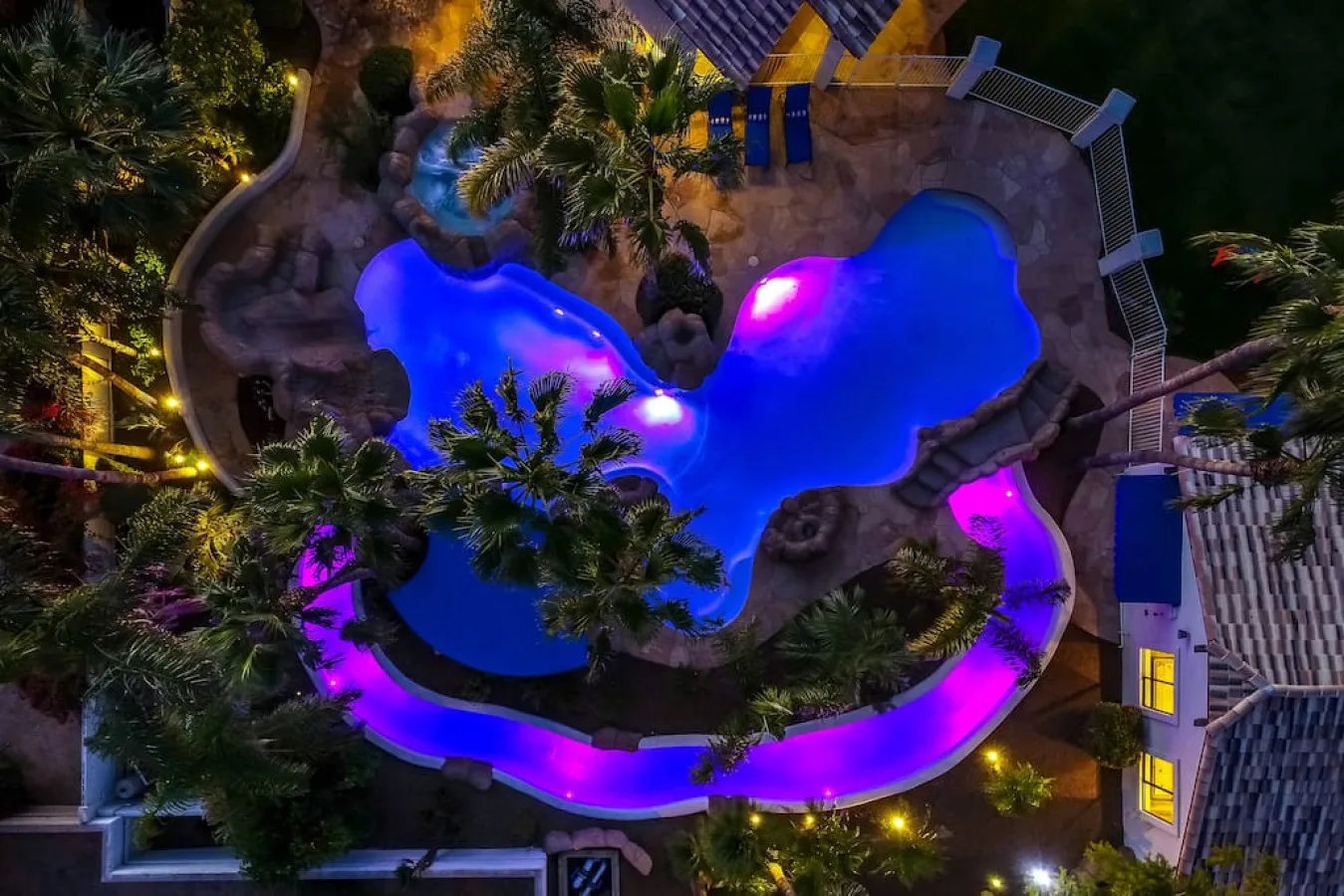 An illuminated swimming pool winds through landscaped grounds at night.
