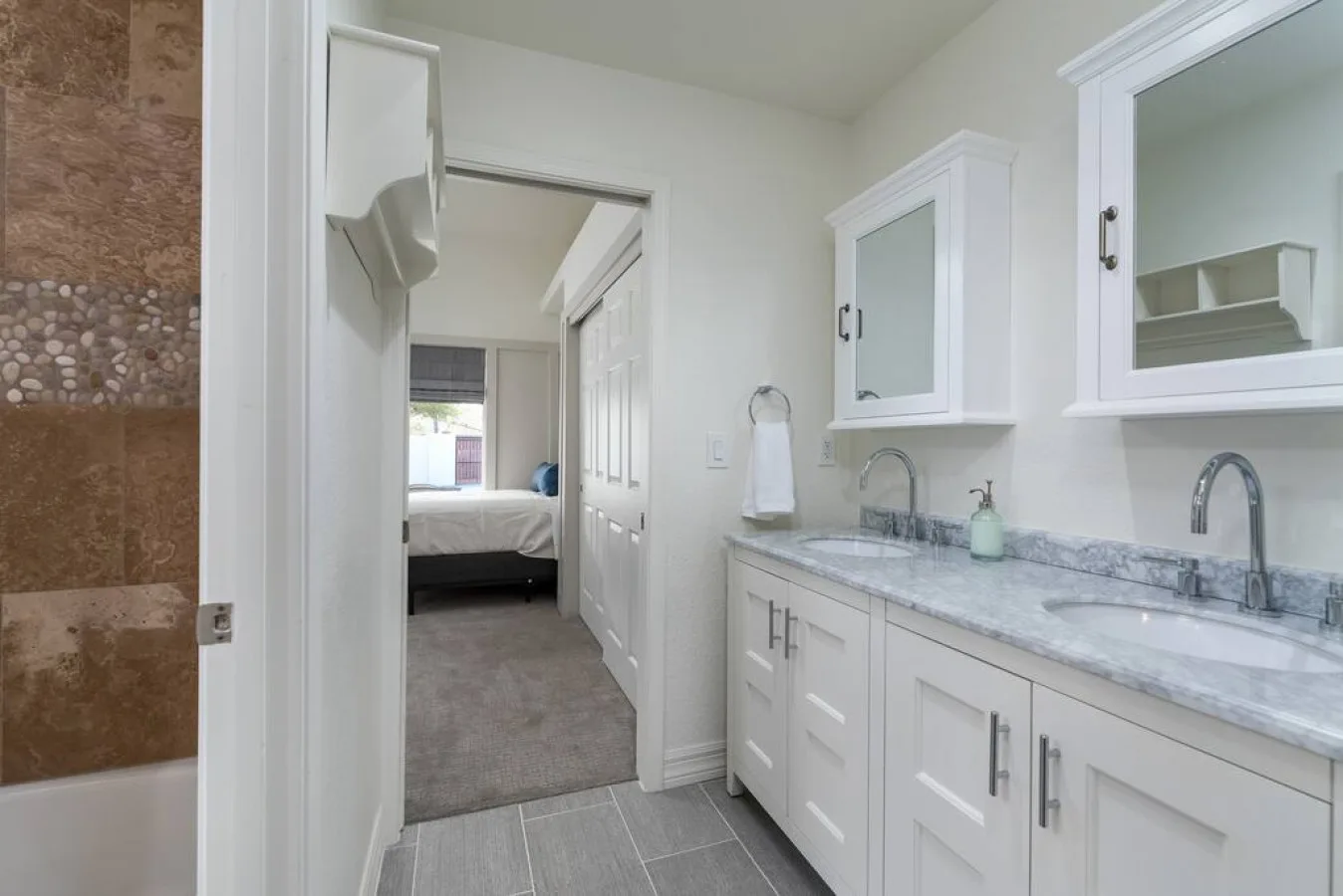Un tocador de baño con una encimera larga y espejos junto a una puerta abierta.