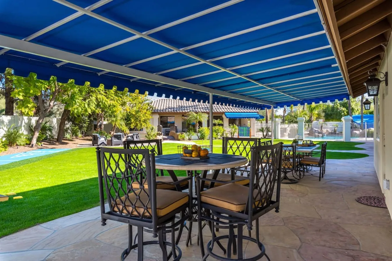 Una zona de comedor exterior con sombra da a una piscina y un césped.
