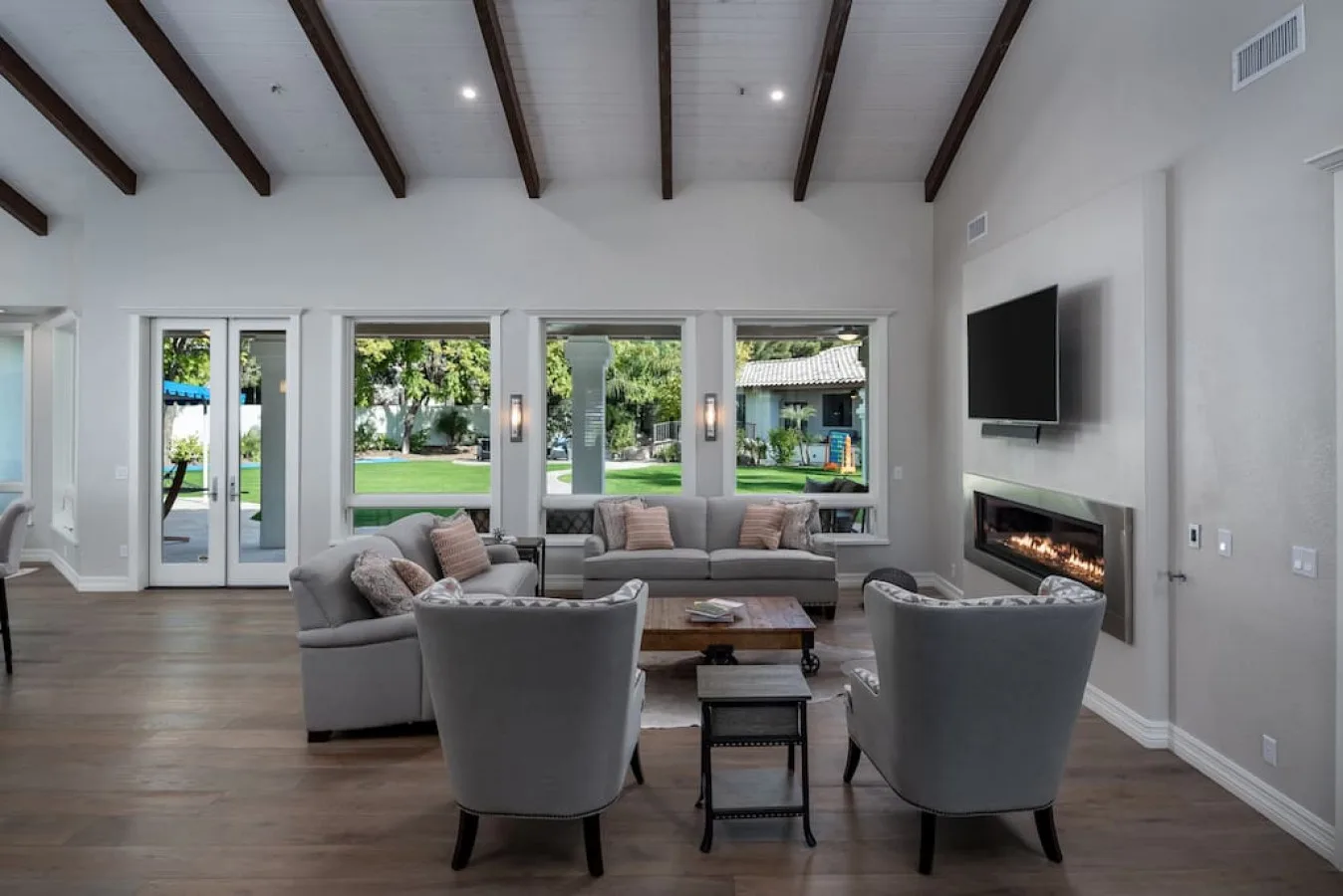 Una sala luminosa con asientos, ventanas grandes y un televisor en la pared.